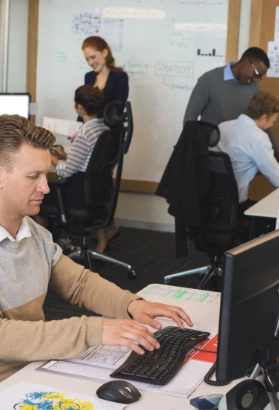 Businessman typing on keyboard while colleagues working in background